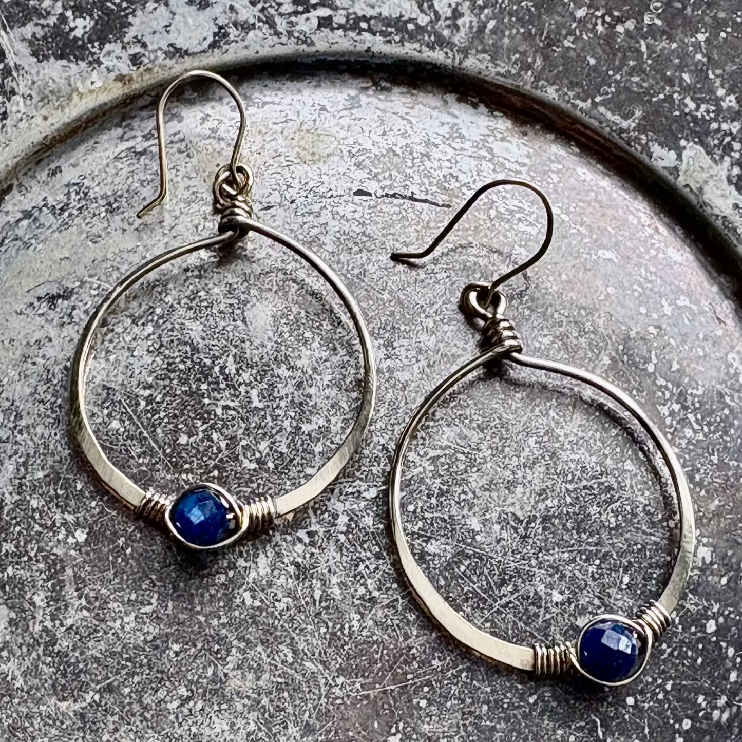 Silver hoop earrings with blue stones on a textured surface