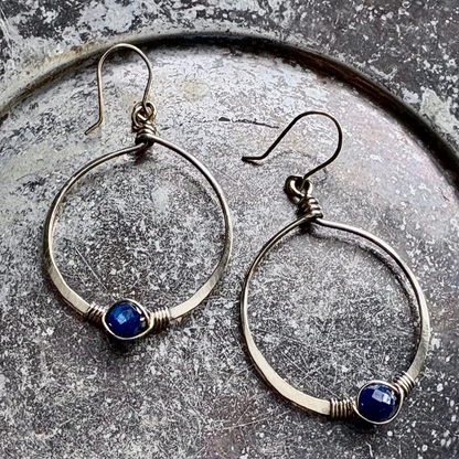 Silver hoop earrings with blue stones on a textured surface