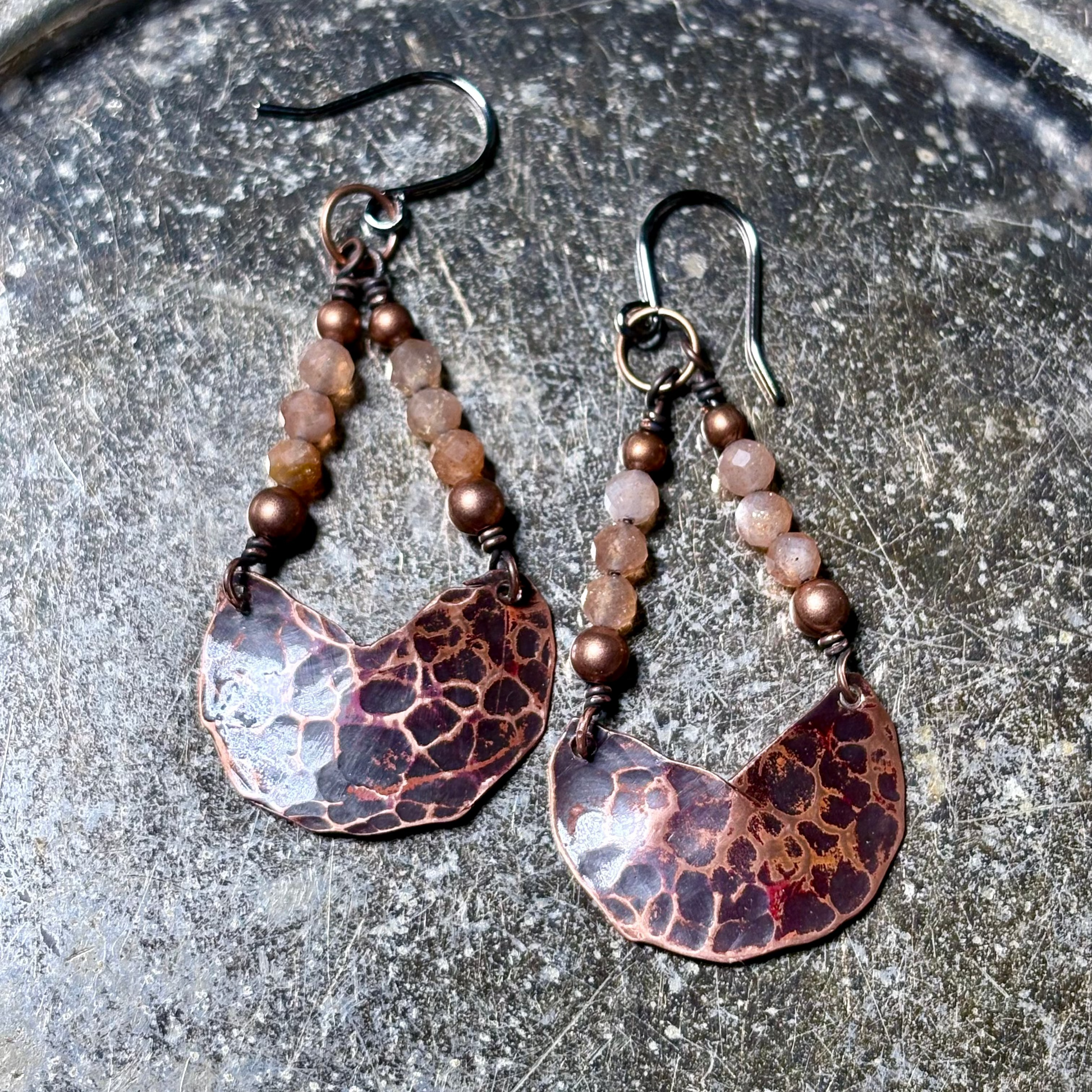 Pair of copper and bead earrings on a textured surface