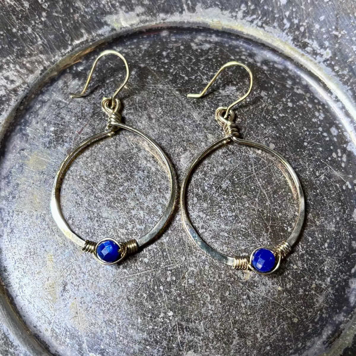 Silver hoop earrings with blue stones on a textured metal surface