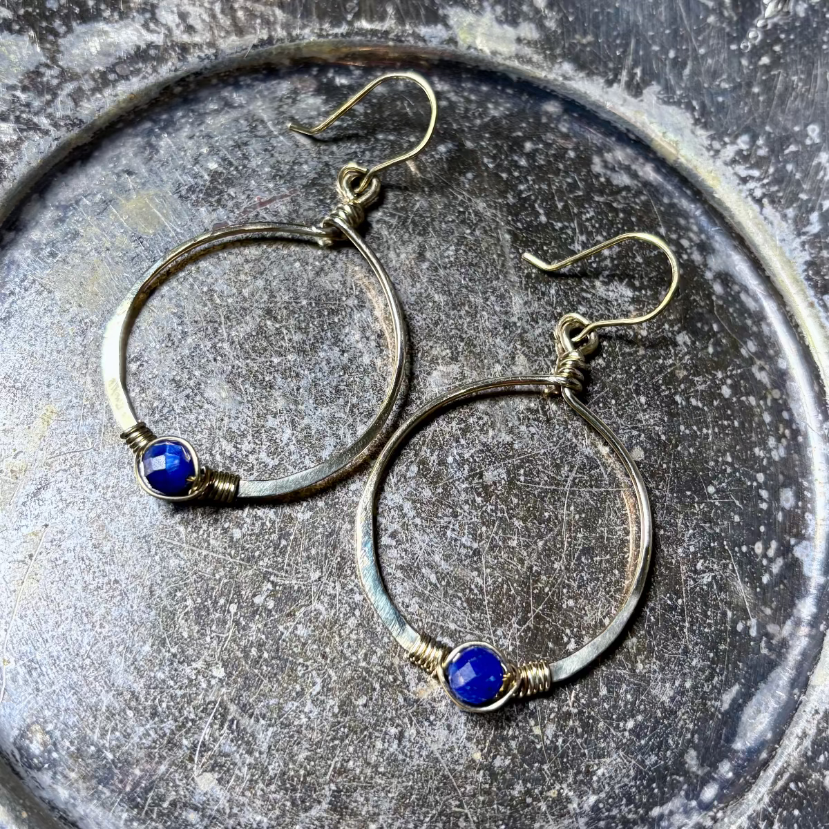 Gold hoop earrings with blue stones on a textured metal surface