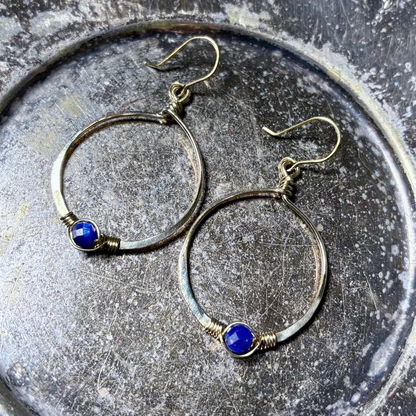Gold hoop earrings with blue stones on a textured metal surface
