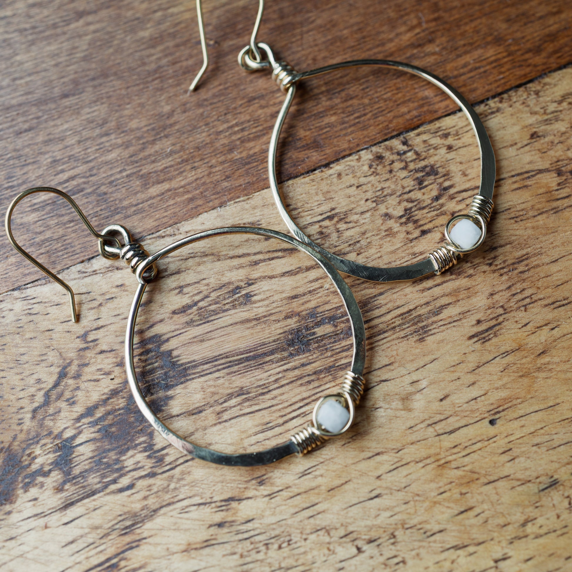 Gold hoop earrings with small stones on a wooden surface